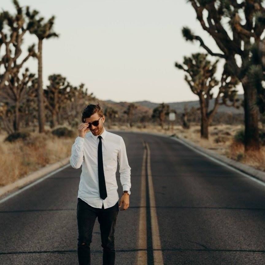 joshua cross in Joshua Tree National Park, California wearing a white dress shirt black tie and black pants standing in the middle of the road with sunglasses