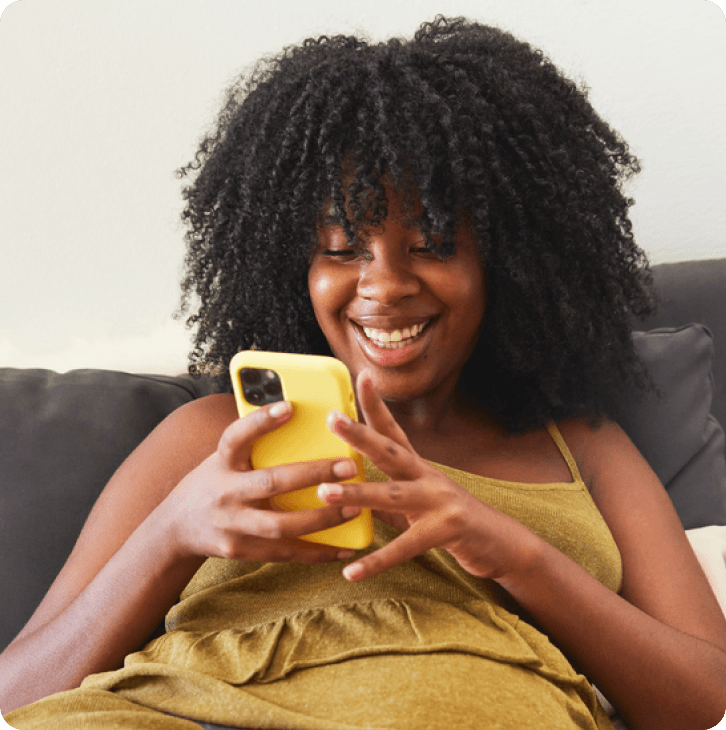 woman on mobile device sitting on the coach looking at her phone smiling