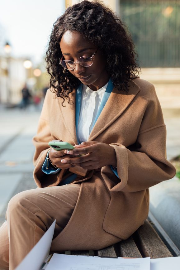 business woman in glasses on a park bench in a trench coat texting